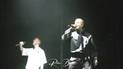 Dos miembros de Hijos de la Ruina cantan micrófono en mano en el escenario en penumbra del Multiusos Sánchez Paraíso