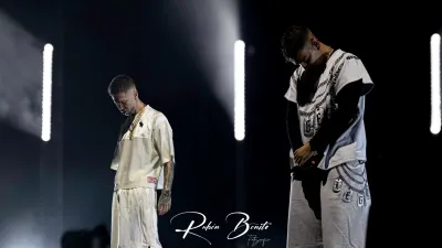 Dos miembros de Hijos de la Ruina, vestidos de blanco, con la cabeza agachada sobre el escenario entre focos y humo