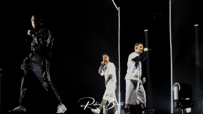 Natos, Waor y Recycled J, de Hijos de la Ruina, cantan sobre un escenario oscuro con columnas de luz blanca en Salamanca