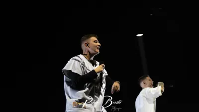 Dos raperos de Hijos de la Ruina, vestidos de blanco, cantan con micrófono sobre un escenario oscuro en el Multiusos de Salamanca