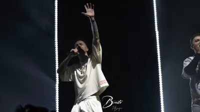 Rapero de Hijos de la Ruina, vestido de blanco, canta con el brazo en alto en el Multiusos Sánchez Paraíso de Salamanca