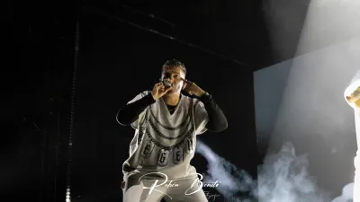 Un miembro de Hijos de la Ruina rapea con camiseta blanca de cadenas y humo en el escenario del Multiusos Sánchez Paraíso