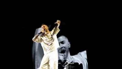 Cantante de Hijos de la Ruina, vestido de blanco, canta con el brazo en alto ante una pantalla con su imagen en blanco y negro