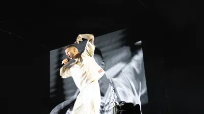 Rapero de Hijos de la Ruina vestido de blanco canta con el brazo en alto ante una pantalla gigante en el Multiusos de Salamanca