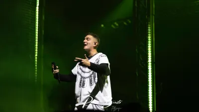 Cantante de Hijos de la Ruina con camiseta blanca de cadenas canta con micrófono bajo luces verdes en el Multiusos de Salamanca