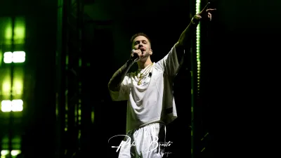 Integrante de Hijos de la Ruina canta con camiseta blanca y cadenas doradas, brazo en alto, en el Multiusos Sánchez Paraíso