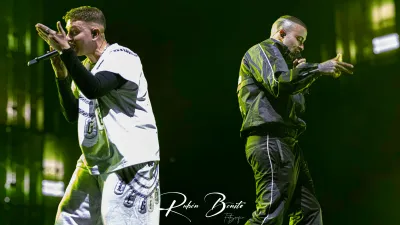 Dos raperos de Hijos de la Ruina cantan con micrófono sobre un escenario iluminado en verde, uno de blanco y otro de negro